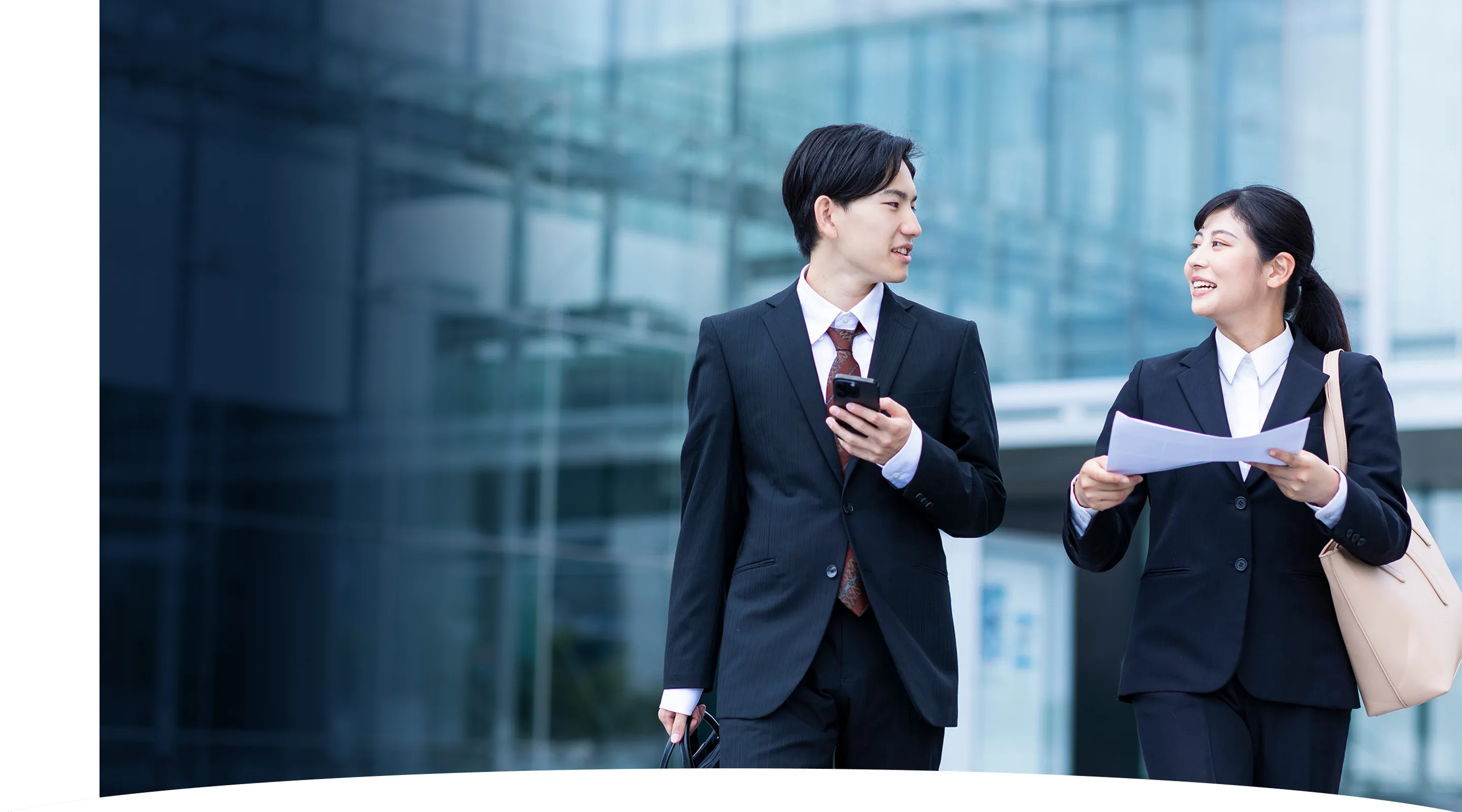 スーツ姿の若い男女社員がオフィスビルの前で会話している